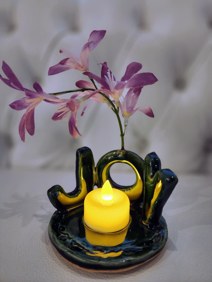 Deep green JOY tea-light holder with a lit candle and lilies