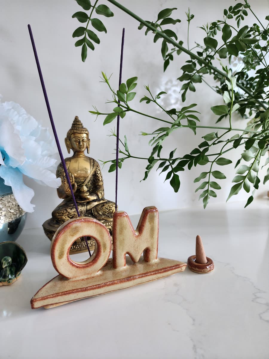 Cream OM incense holder beside a brass Buddha